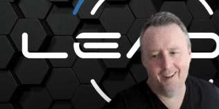 A man with short hair smiles in front of a black hexagonal patterned background featuring the word "LEAD" in white text.