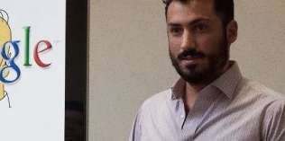 A man with a beard and mustache stands next to a poster displaying part of the Google logo.